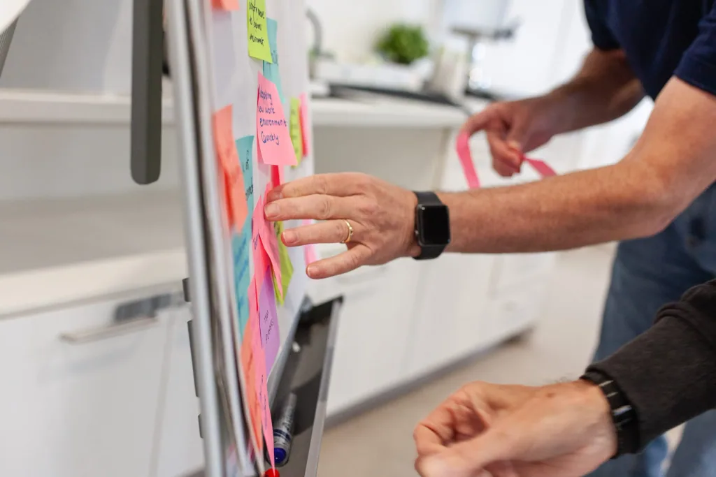 Close-up of hands arranging sticky notes on a whiteboard while mapping a delivery workflow